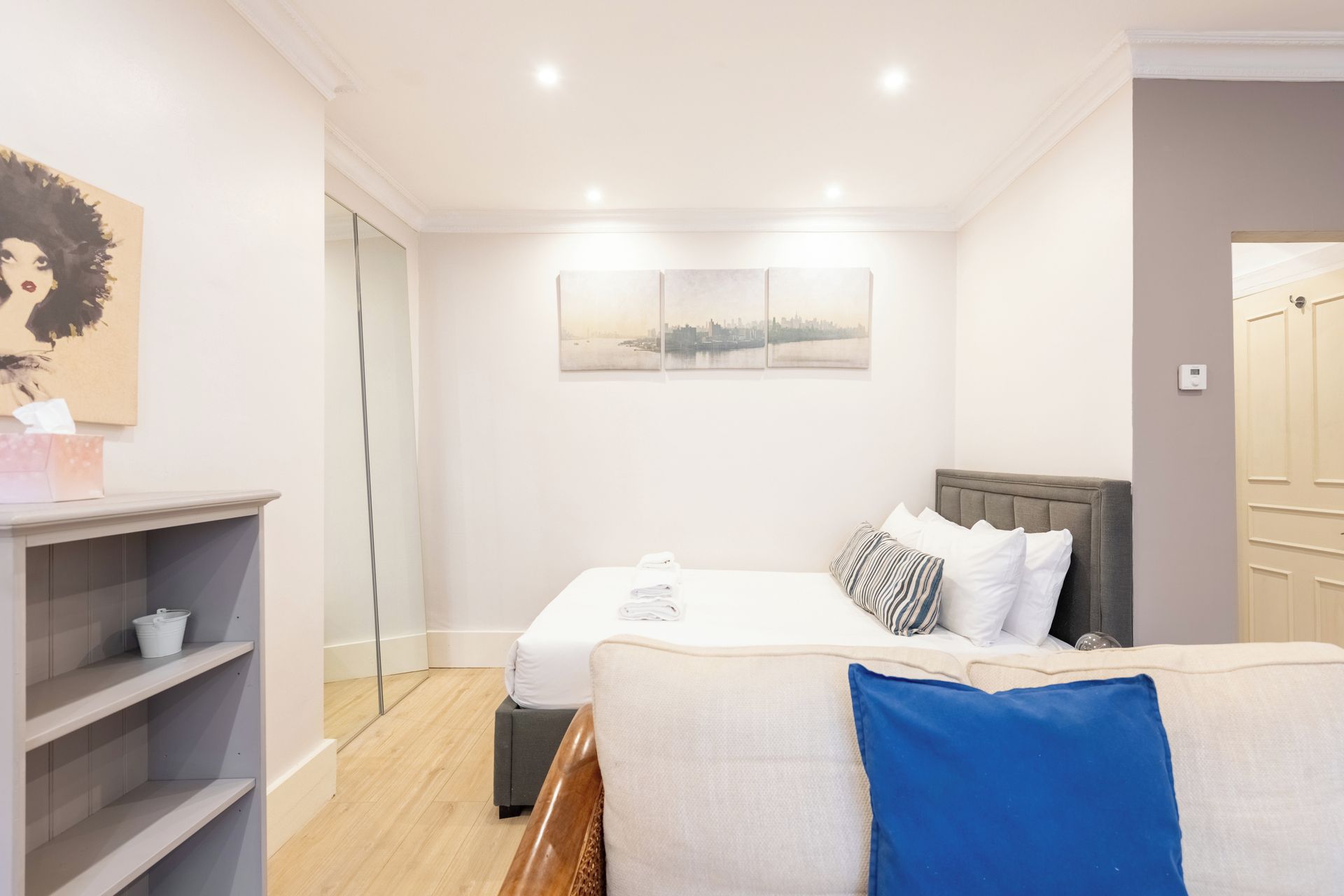 Une chambre d’hôtel avec un lit, une table de chevet, une chaise, une fenêtre donnant sur la ville et un tableau au mur.