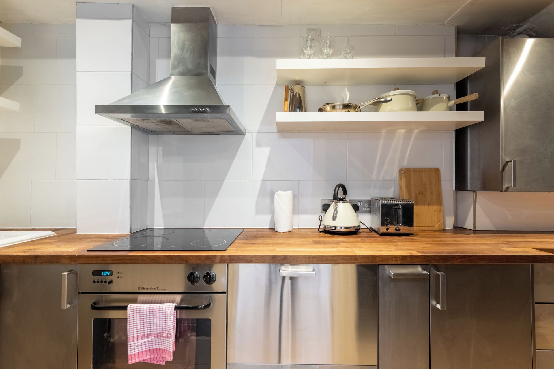 A modern kitchen with stainless steel appliances, a wooden countertop, and white tiled walls.