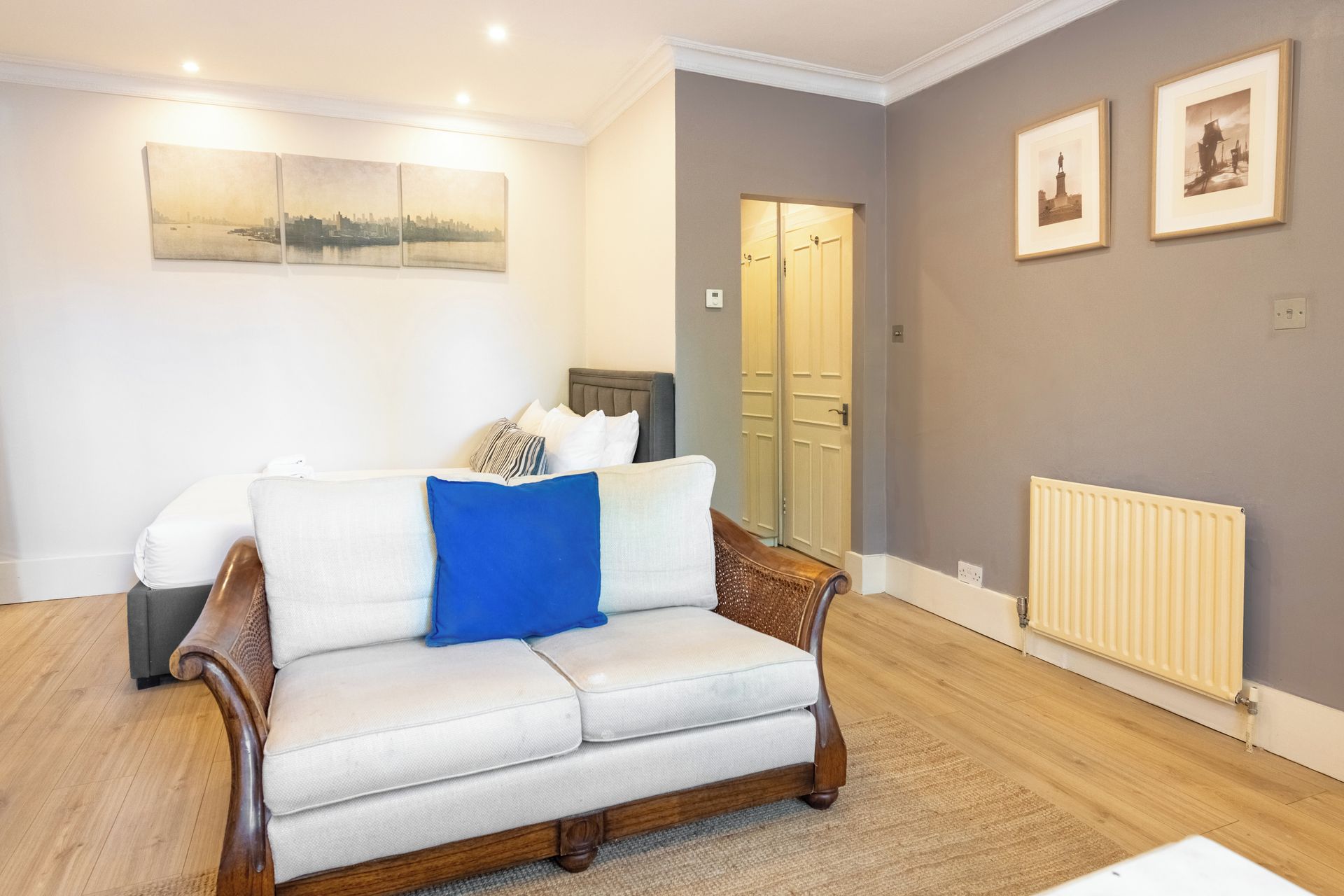 A room with a sofa, a radiator, and framed pictures on the wall.