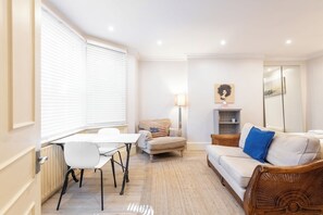 A well-lit living room with a dining area, a sofa, a chair, and a lamp. - Chic Studio Retreat by Portobello Road (Greater London)