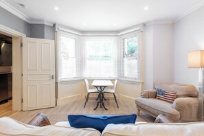 Una habitación con ventana de esquina, una mesa de comedor con sillas, un sofá y una lámpara.