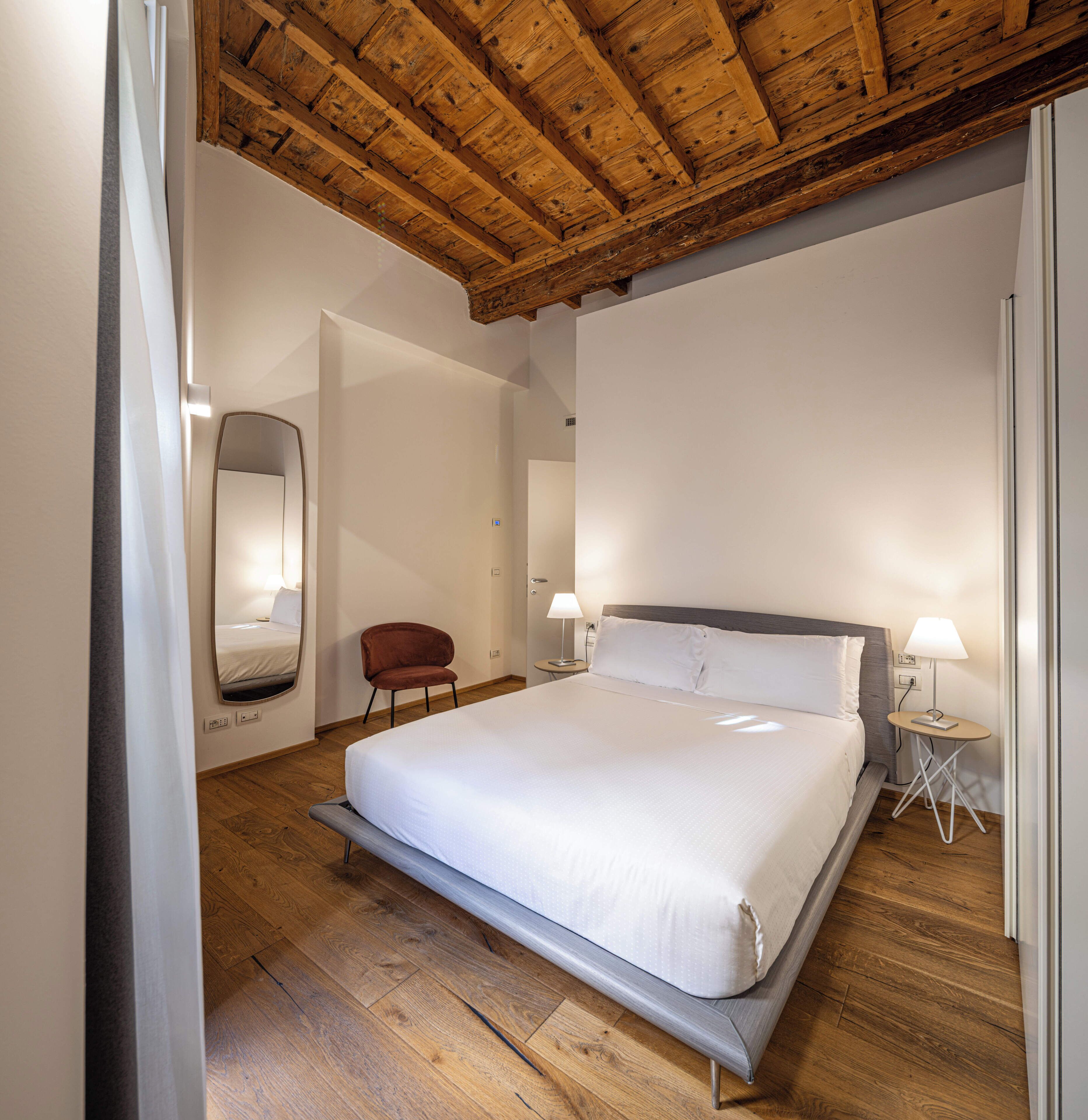 Een slaapkamer met een groot bed, een stoel, een nachtkastje en een houten plafond.
