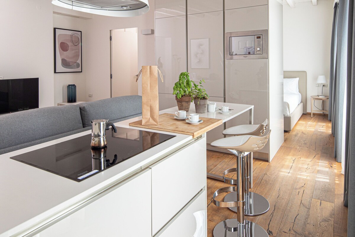 Una cocina moderna con una isla central, un comedor con un taburete de bar y una sala de estar con sofá y televisor.