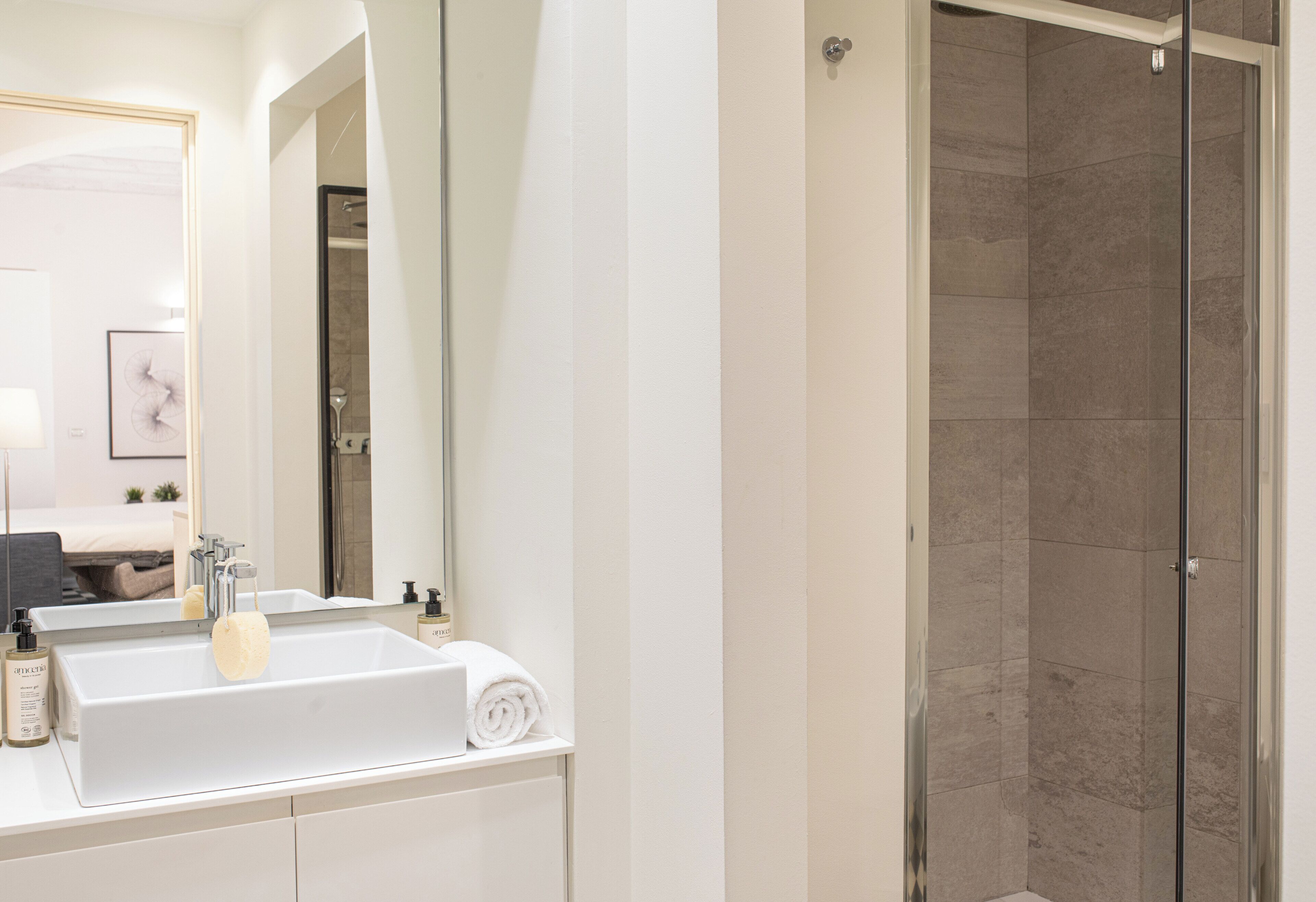 A modern bathroom with a white sink, a mirror, and a glass shower enclosure.