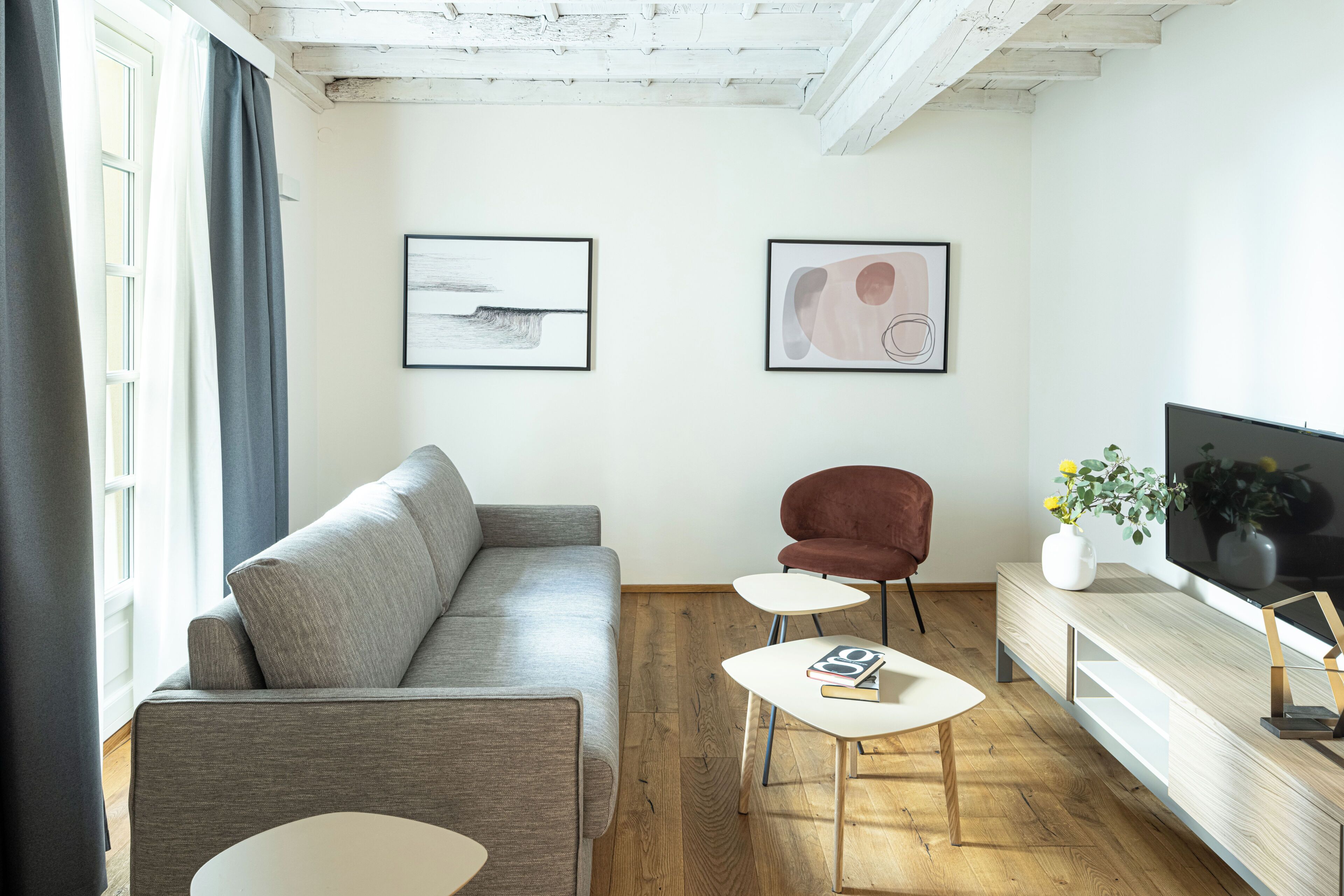 Un moderno salón con un sofá gris, un sillón rojo, una mesa de centro blanca y un televisor de pantalla plana sobre un mueble de madera.