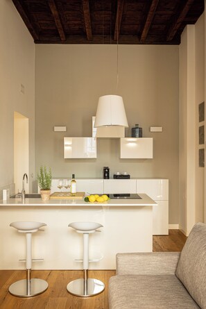 Una cocina moderna con una isla central, taburetes de bar, una lámpara colgante y techo de madera.