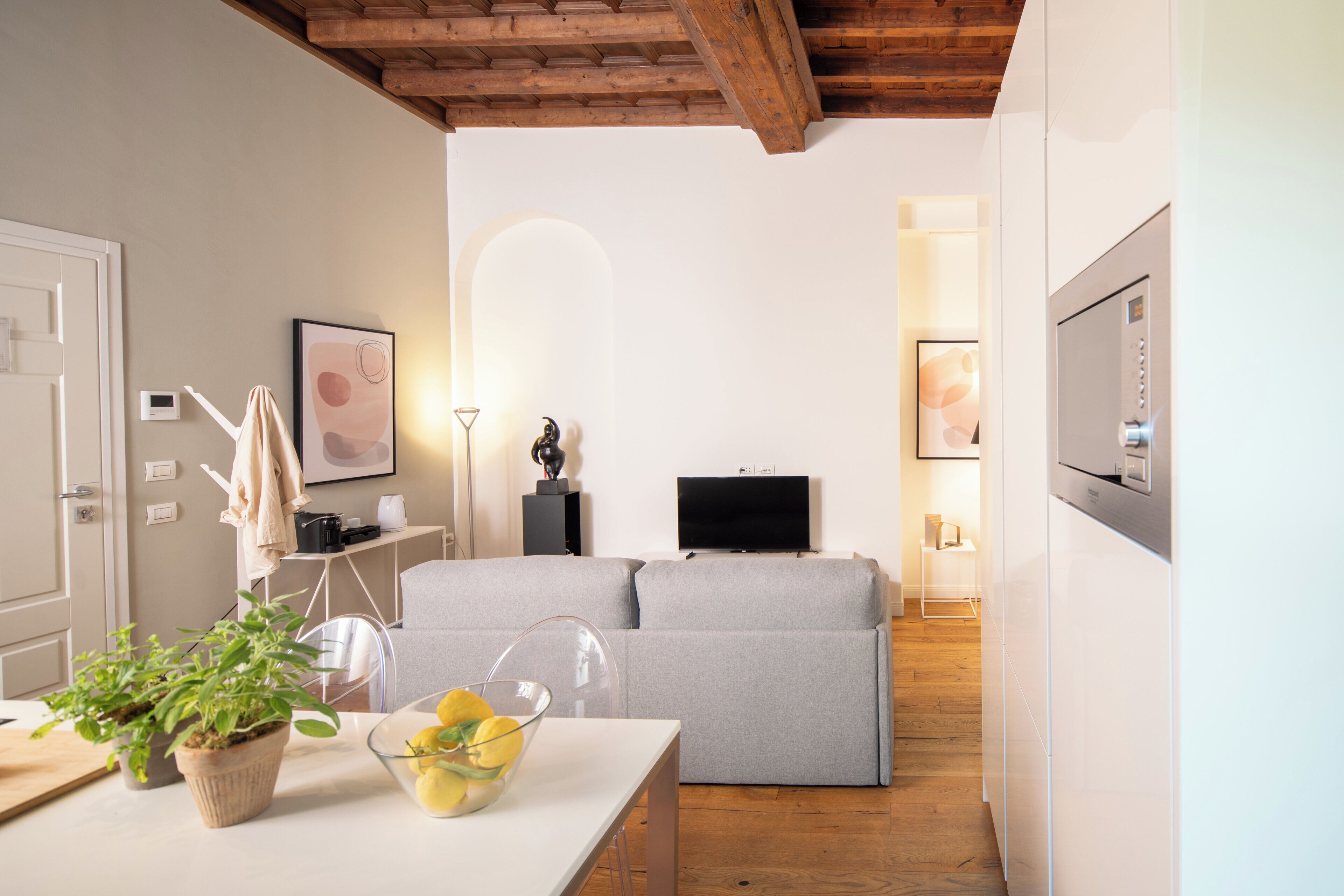 Uma sala de estar moderna com um sofá cinzento, uma mesa de centro com uma tigela de vidro, uma televisão e teto de madeira.