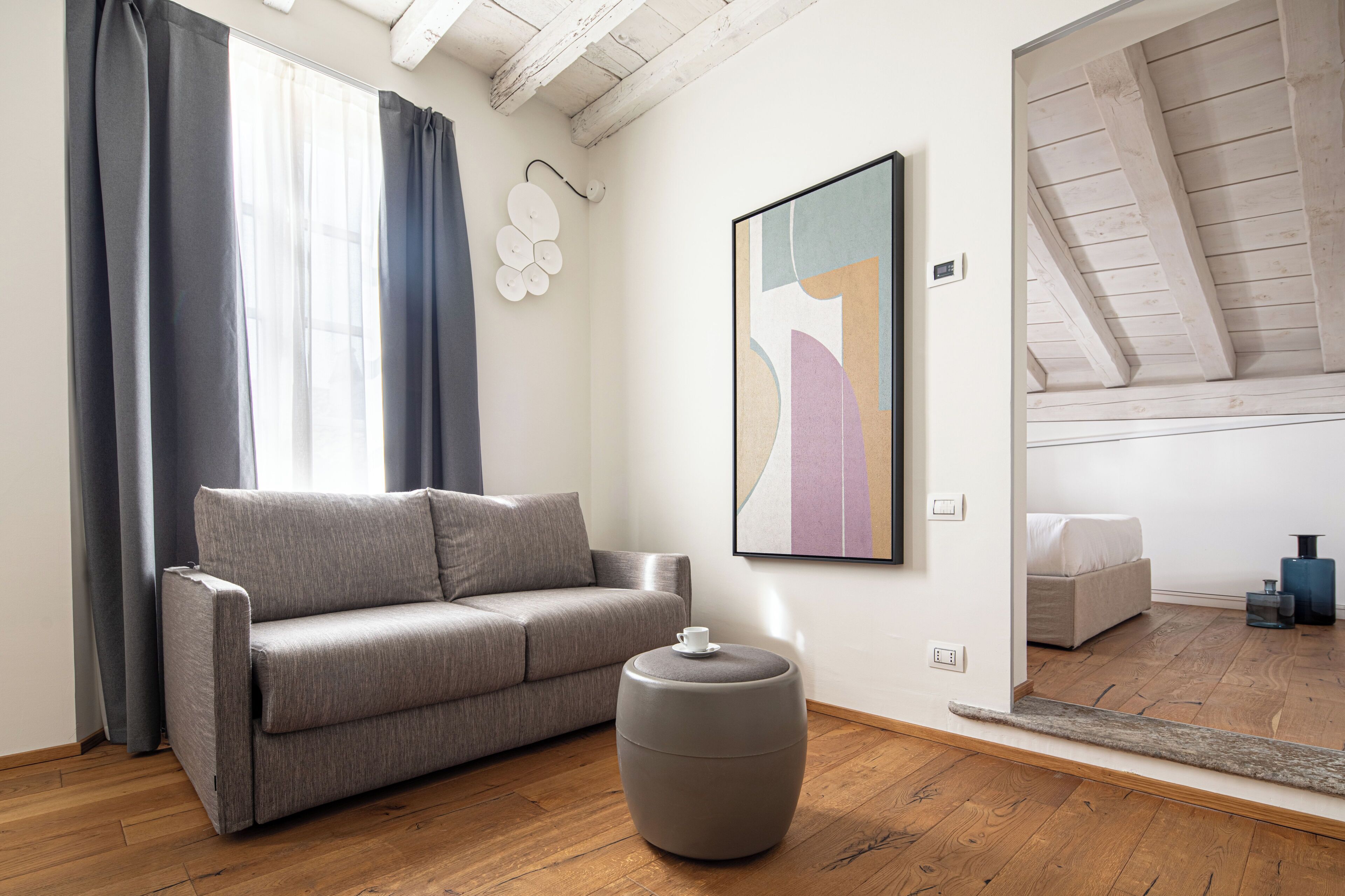 Ein modernes Wohnzimmer mit einem grauen Sofa, einem runden Ottomanen und einem großen abstrakten Gemälde an der Wand.
