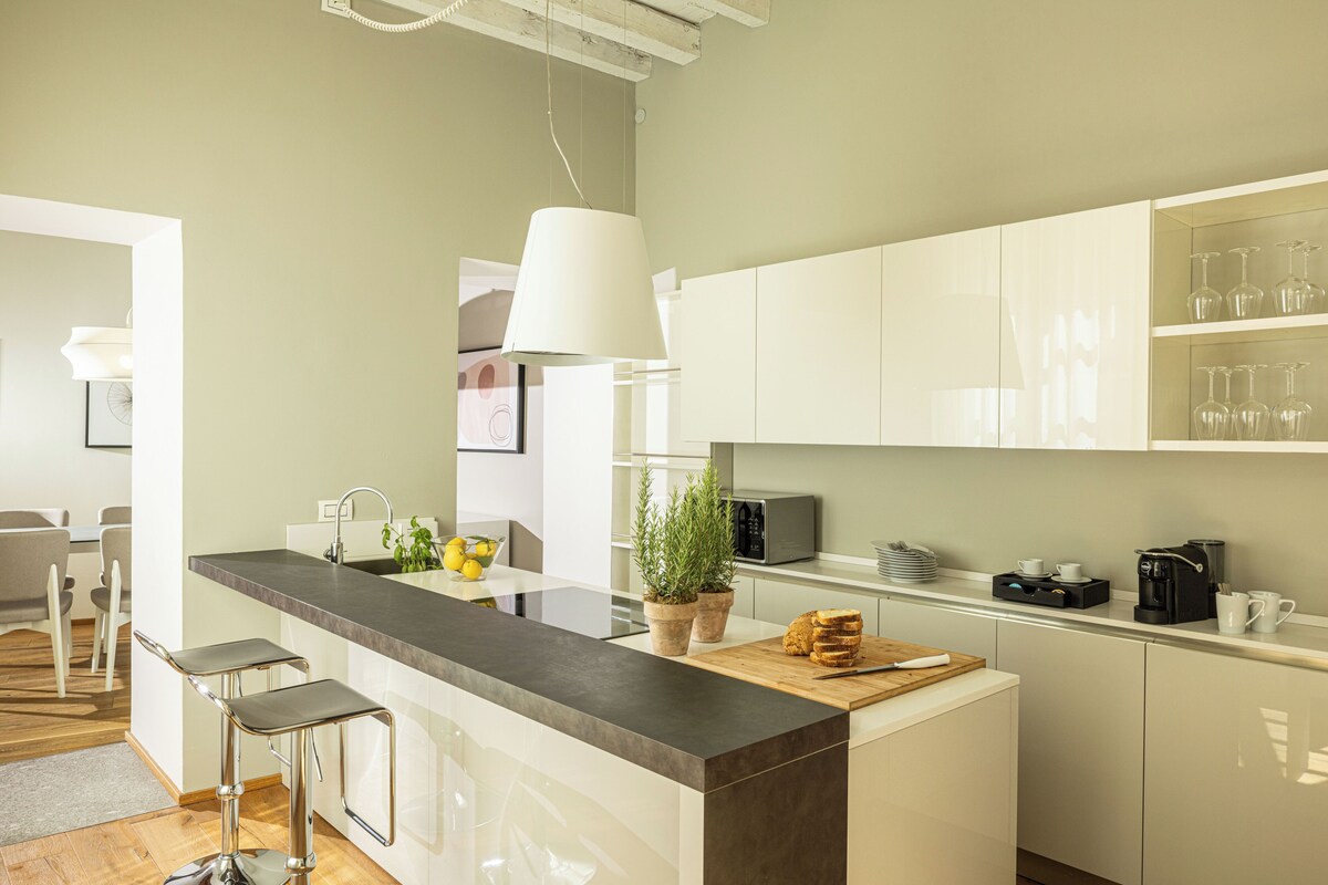 Cocina moderna con una isla central, taburetes de bar, una cafetera y una planta en maceta.
