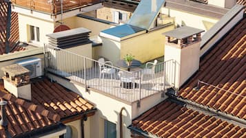 Une terrasse sur le toit, avec une table et des chaises, un pot de fleurs et une vue sur les bâtiments voisins.