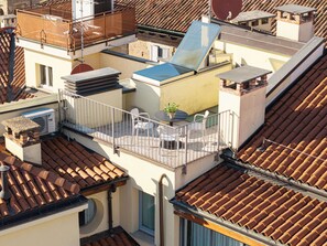 Una terraza en la azotea con una mesa, sillas, una planta en maceta y vistas a edificios cercanos.