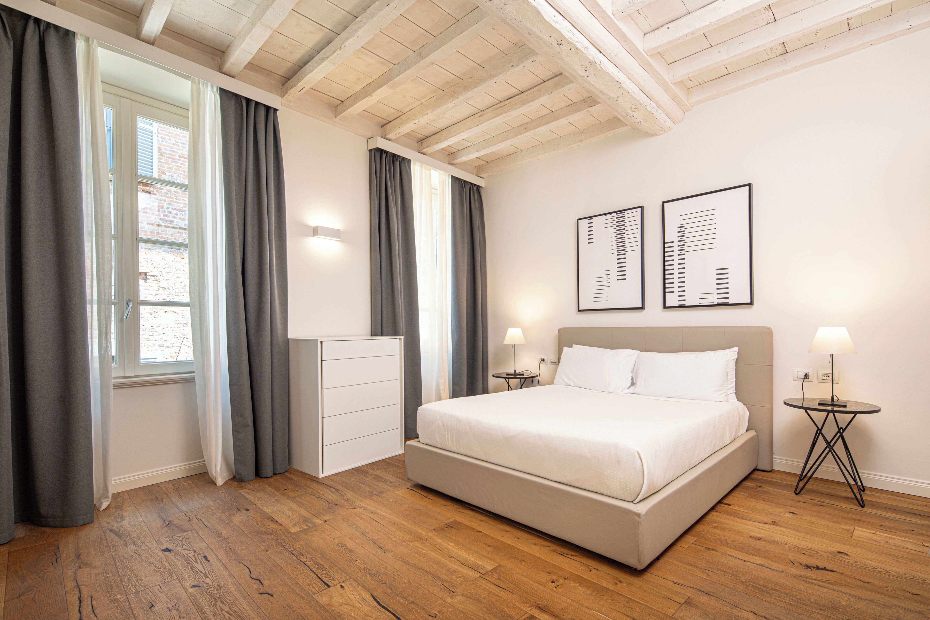 Une chambre à coucher avec un grand lit, une commode, deux tables de chevet avec des lampes et deux œuvres d’art encadrées accrochées au mur.