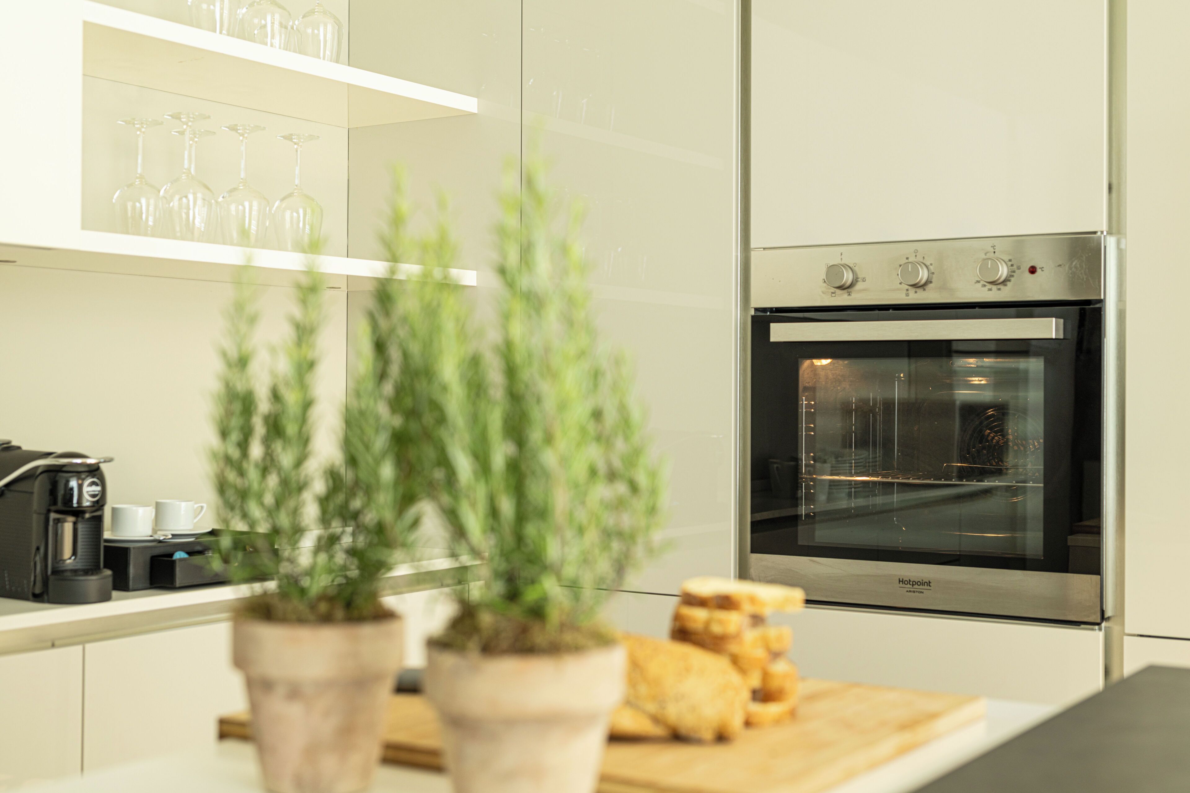 Una cocina moderna con horno empotrado, cafetera y tabla de madera con pan.