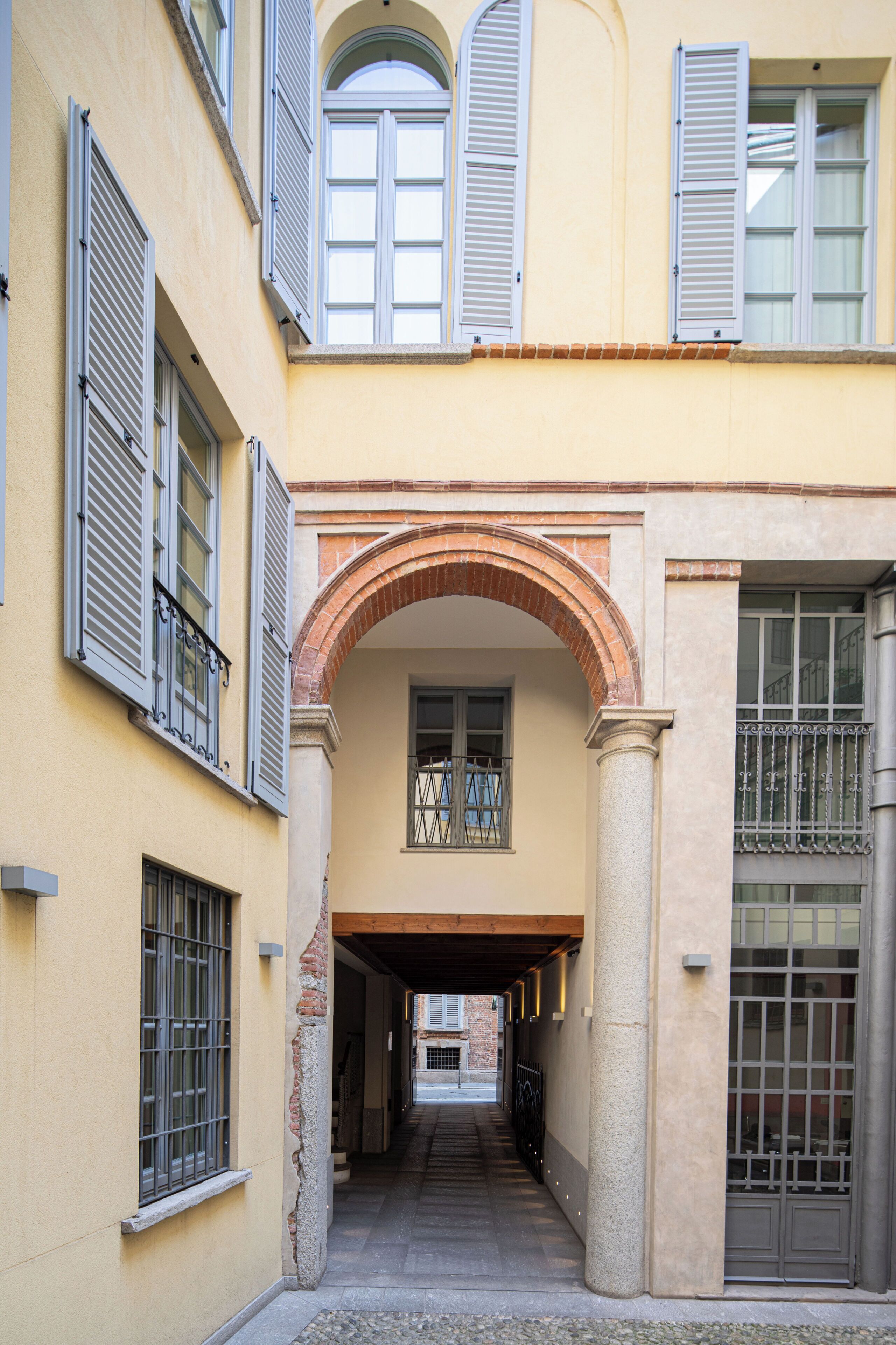 A narrow alleyway with a covered passageway, flanked by buildings with shuttered windows and a central archway.