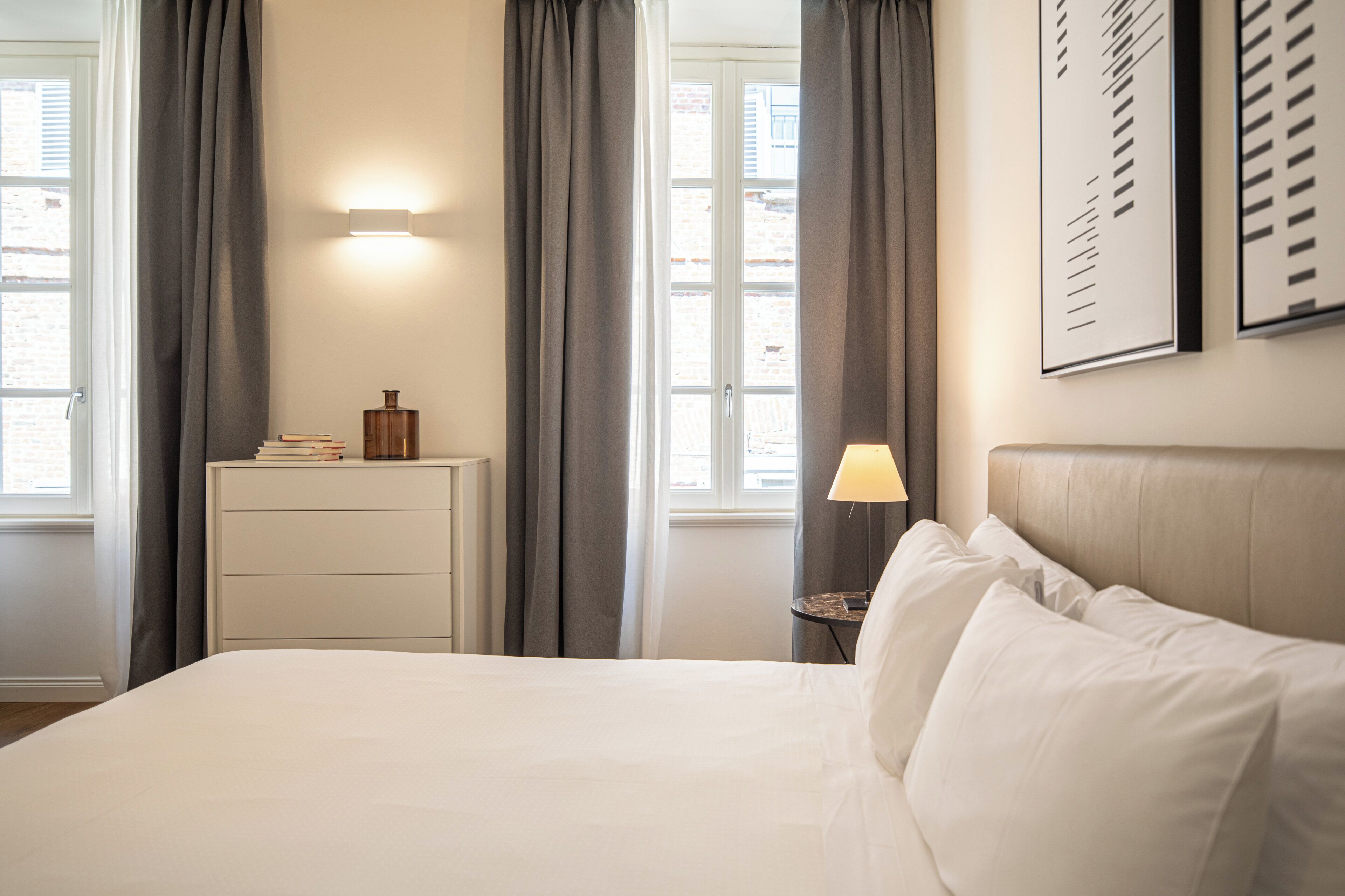 A hotel room with a bed, a nightstand, a lamp, and a window with curtains.