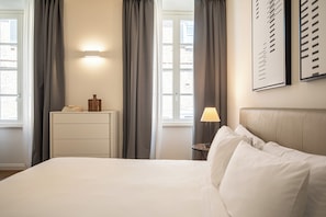 Een hotelkamer met een bed, nachtkastje, lamp en een raam met gordijnen.