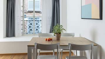 Un coin repas comprenant une table, des chaises, une plante en pot et donnant sur un balcon avec une balustrade.
