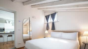 A hotel room with a large bed, a desk with a chair, a mirror, and a window with curtains.
