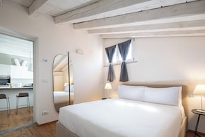 Habitación de hotel con una cama grande, un escritorio con silla, un espejo y una ventana con cortinas.