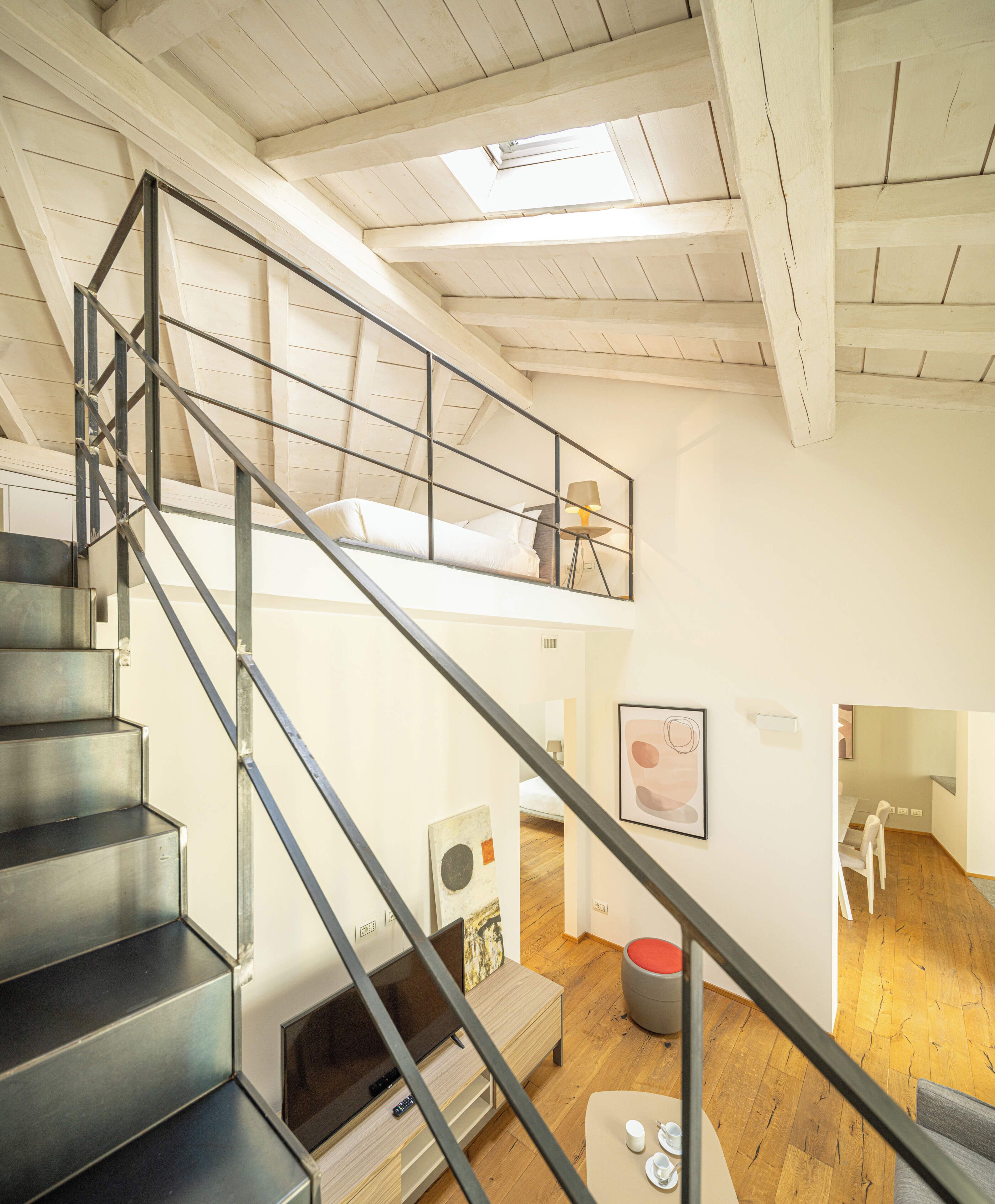 A multi-level interior with a staircase, a loft bedroom, a dining area, and a living space.