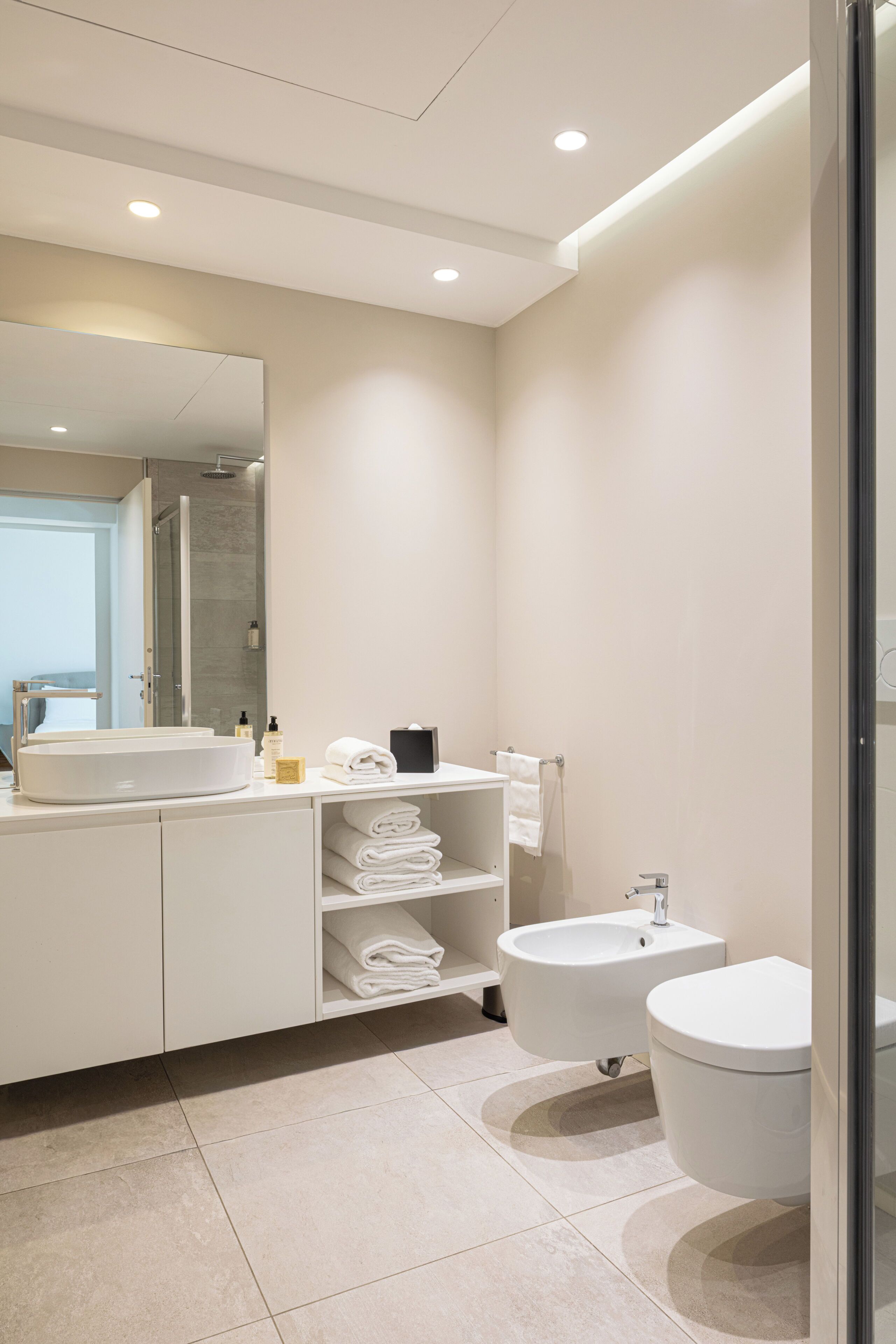 A modern bathroom with a large mirror, a sink, a bidet, and neatly folded towels.