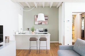 Een moderne keuken met een centraal eiland, barkrukken, een hanglamp en een koffieapparaat.