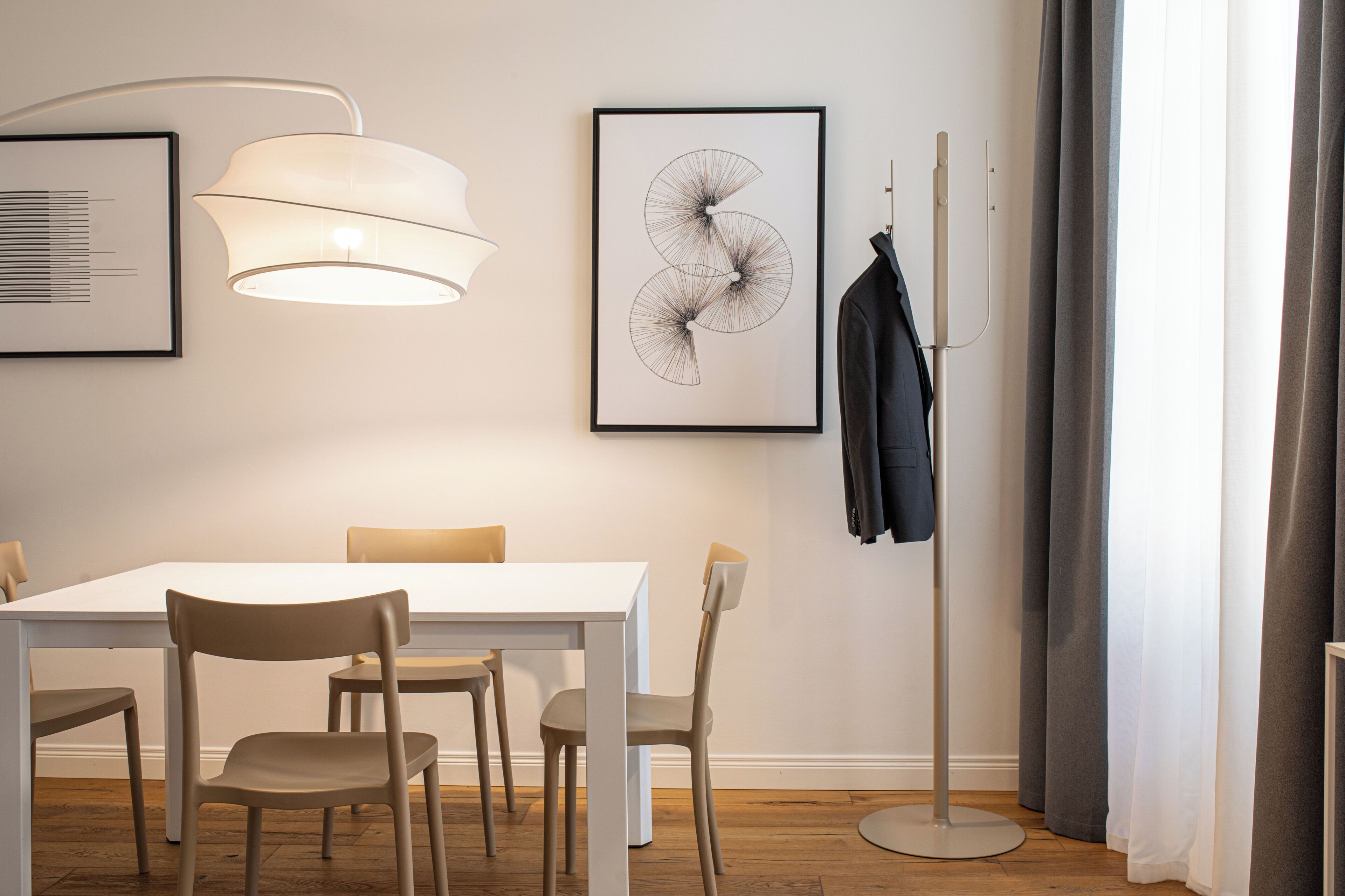 A modern dining area with a white table and chairs, a floor lamp, and two framed artworks on the wall.