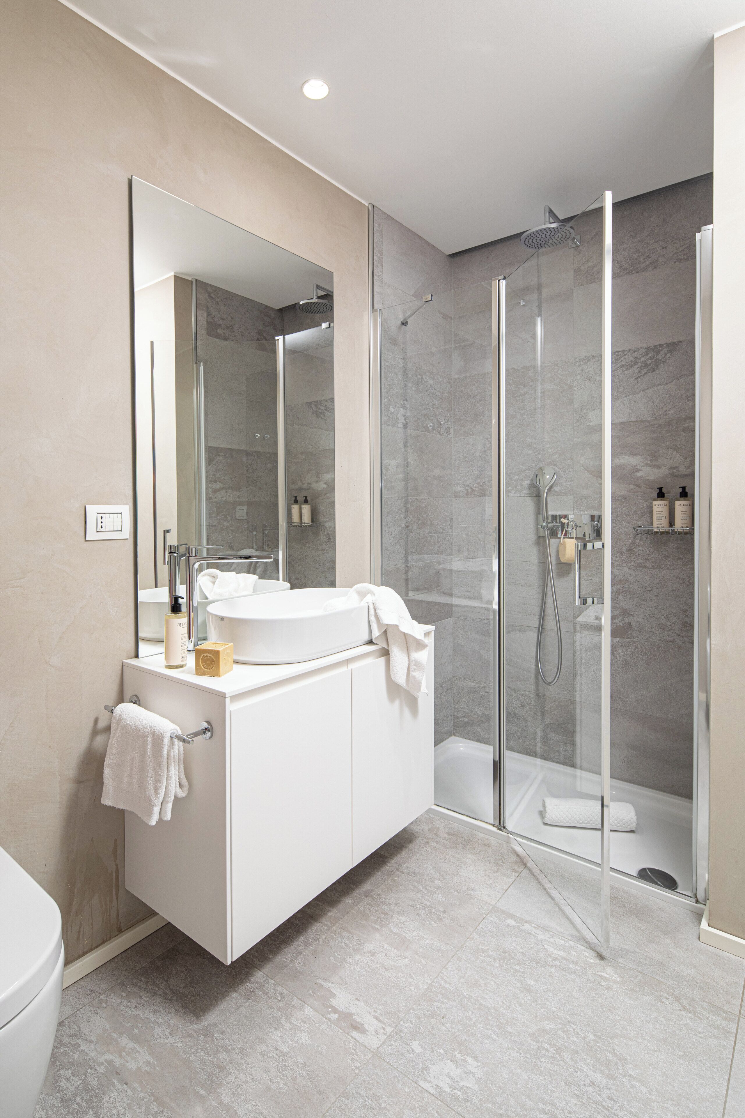 A modern bathroom with a glass-enclosed shower, a white vanity with a large mirror, and a toilet.