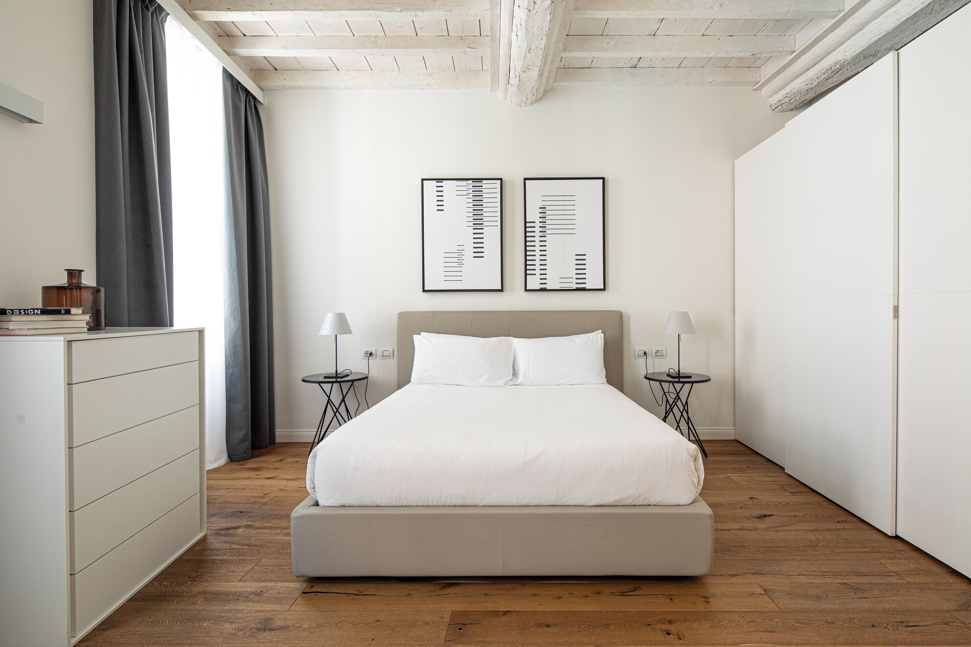 Un dormitorio minimalista con una cama grande, dos mesitas de noche con lámparas, un aparador y dos obras de arte abstracto enmarcadas en la pared.