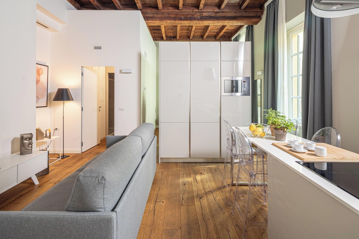 Una cocina moderna con vigas de madera, un sofá gris y un comedor con sillas transparentes y una mesa de madera.