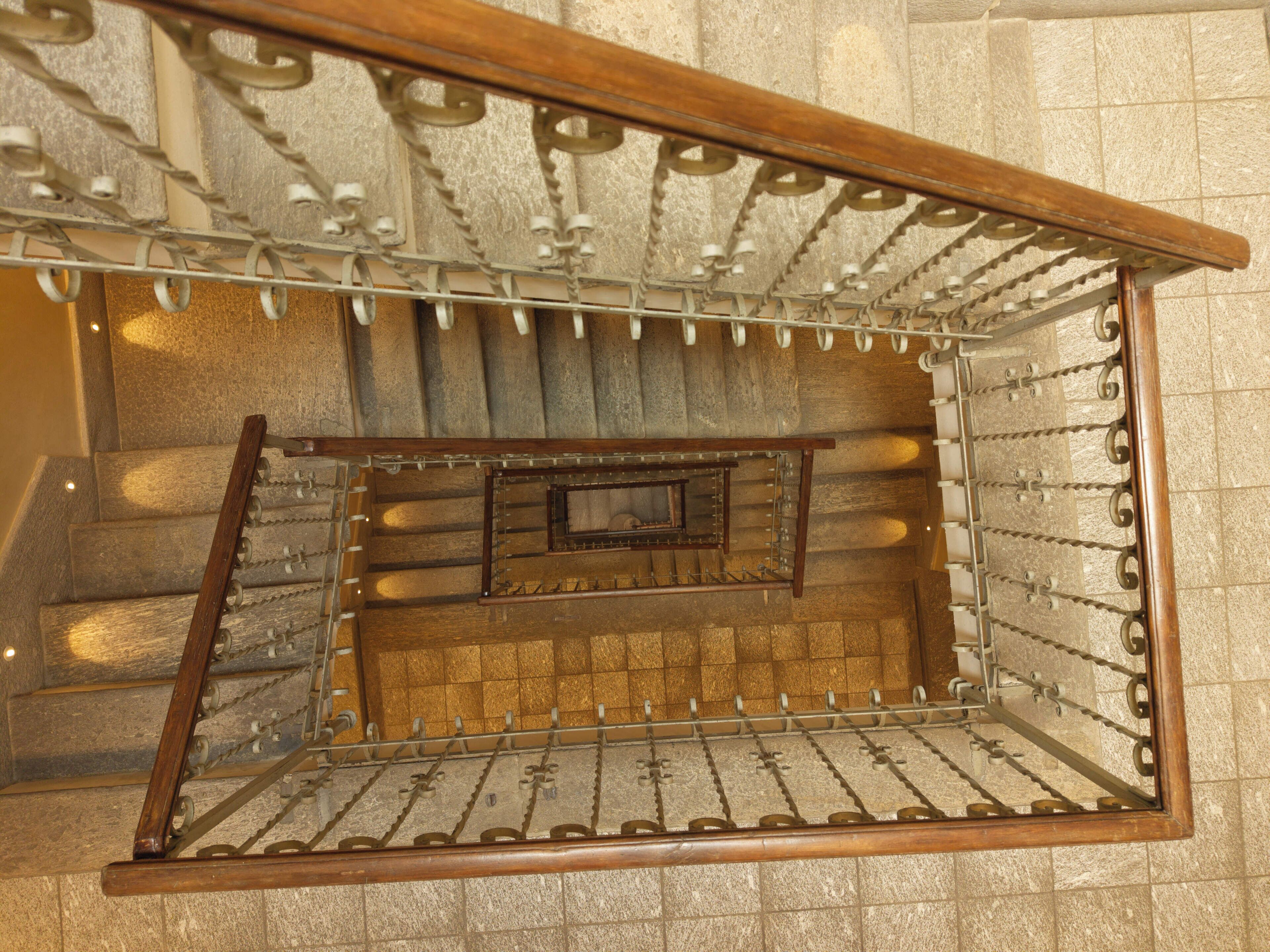 A spiral staircase with a wooden handrail and metal balustrade, leading to an upper level.