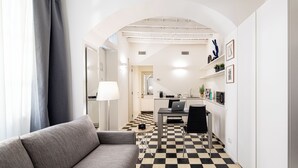 Un interior moderno con piso a cuadros, un sofá, una mesa de comedor con una computadora portátil y una zona de cocina con pileta y alacenas.