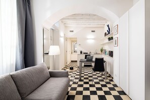 Un interior moderno con piso a cuadros, un sofá, una mesa de comedor con una computadora portátil y una zona de cocina con pileta y alacenas.