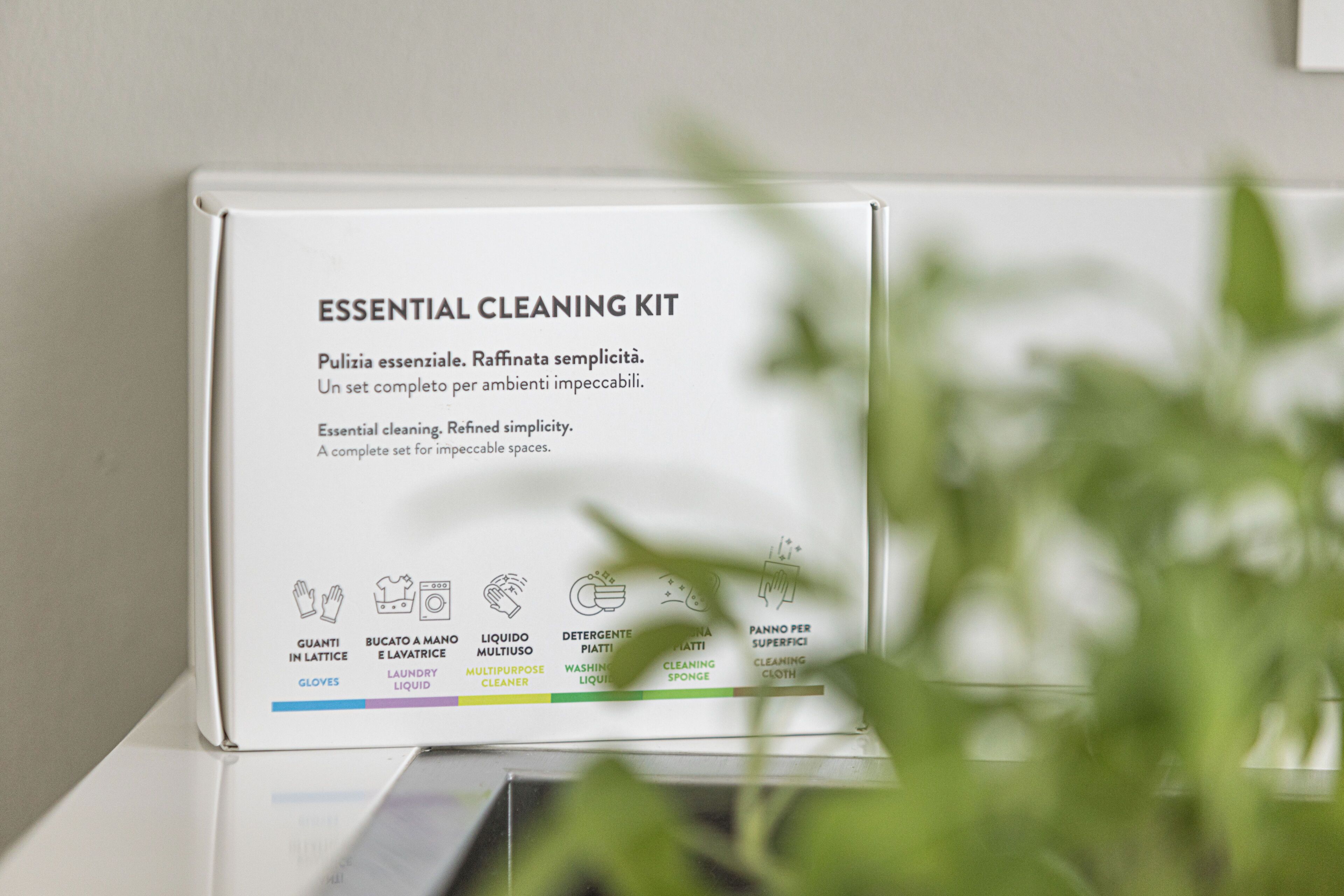 Una confezione bianca di kit pulizia essenziale con testo e icone in italiano per guanti, detersivo per bucato, detergente multiuso, sapone per bucato, spugna e panno.