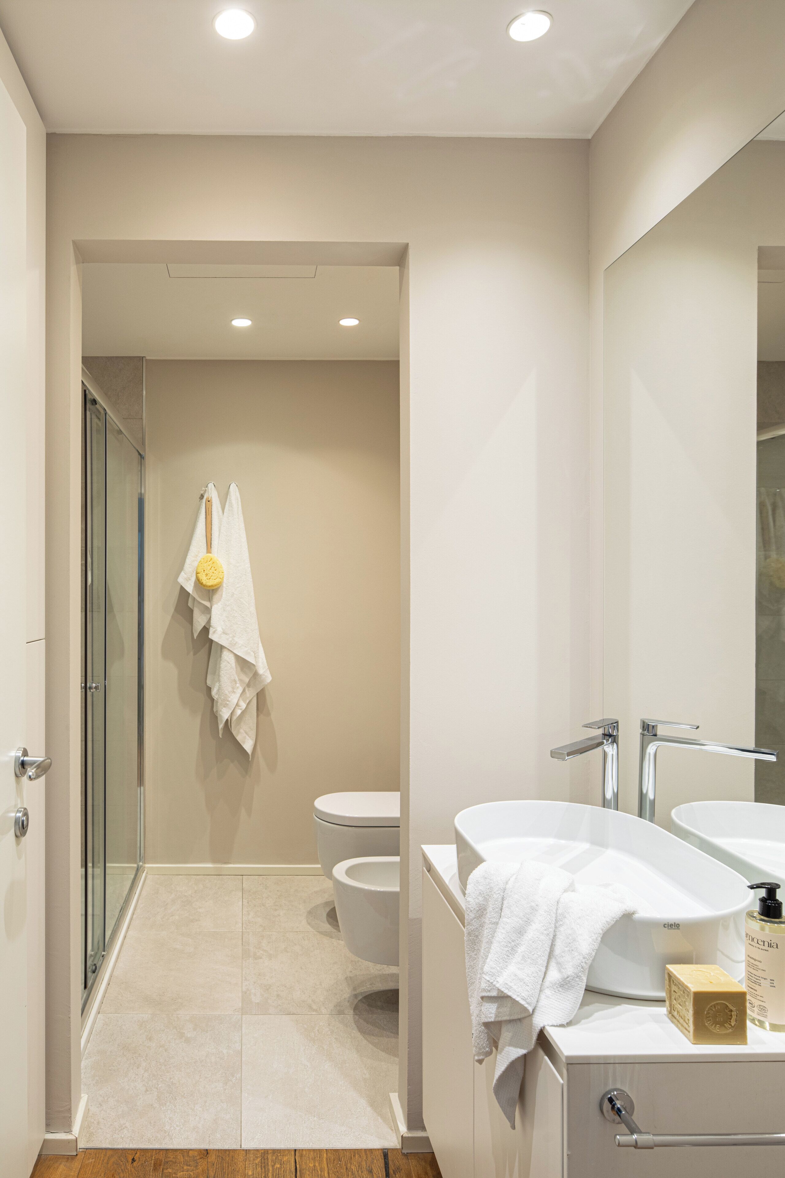 A modern bathroom with a glass shower enclosure, a toilet, a bidet, and a vanity with a mirror.