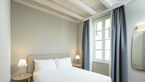 Una habitación de hotel con una cama, mesitas de noche, una lámpara, una ventana con cortinas y un espejo.