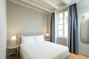 Una habitación de hotel con una cama, mesitas de noche, una lámpara, una ventana con cortinas y un espejo.