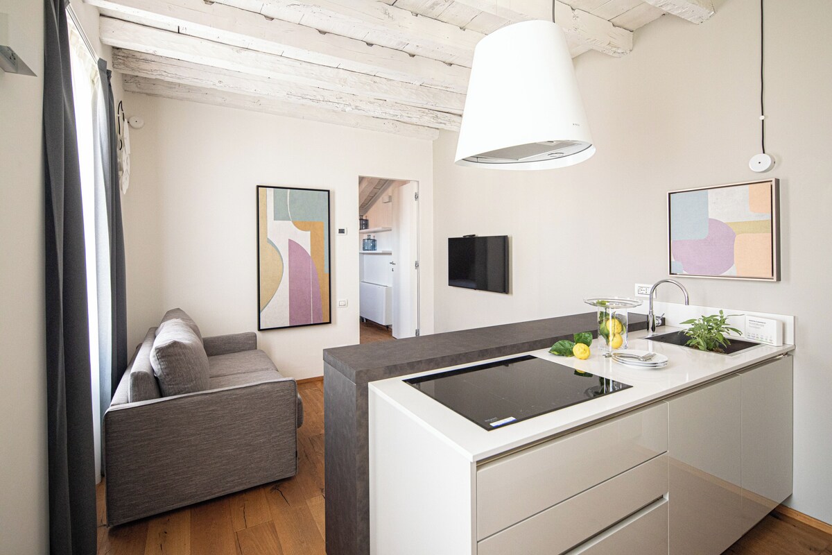 Una cocina moderna con estufa integrada, un comedor con sofá gris y una lámpara colgante.