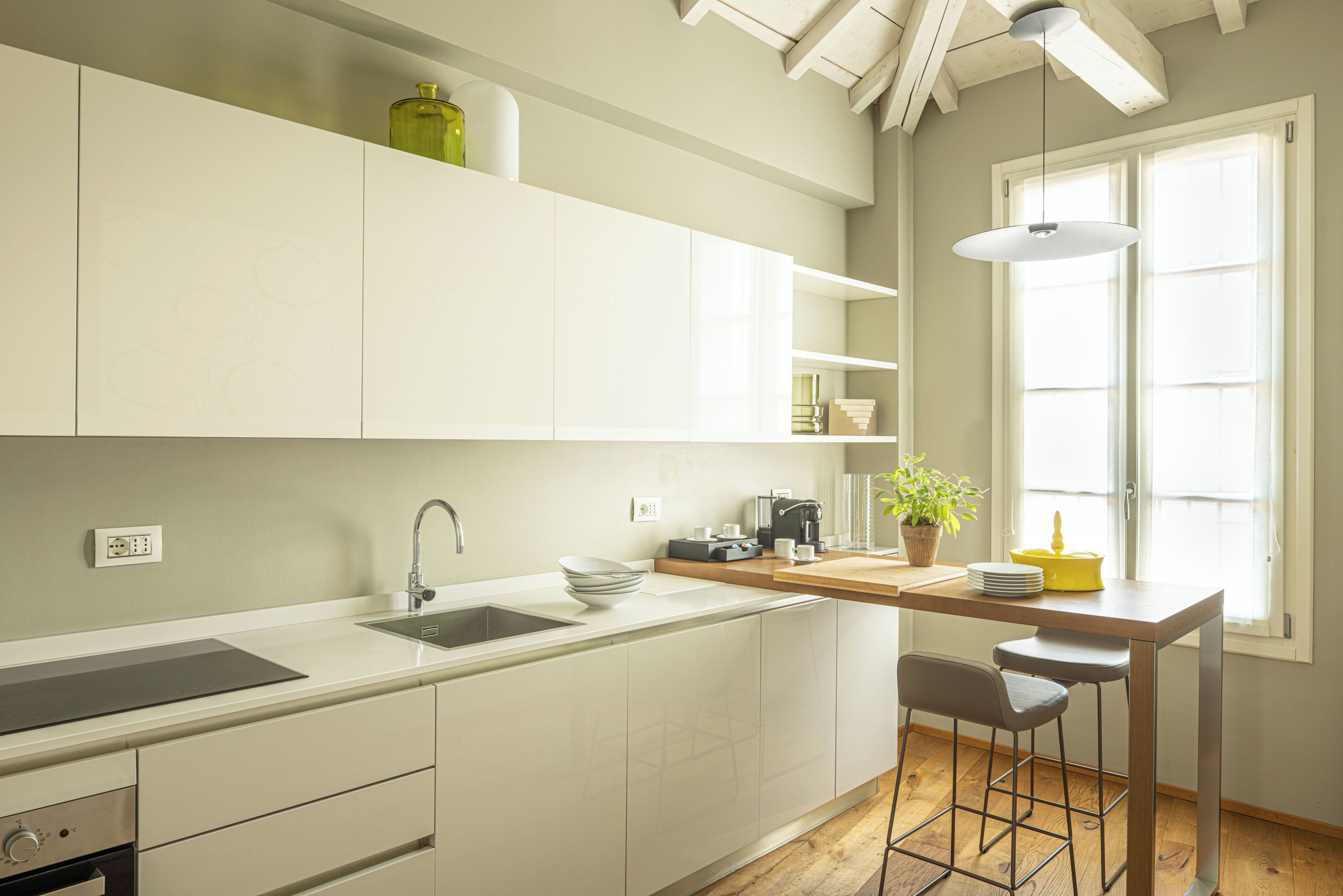 A modern kitchen with white cabinetry, a built-in oven, a sink, and a bar area with stools.