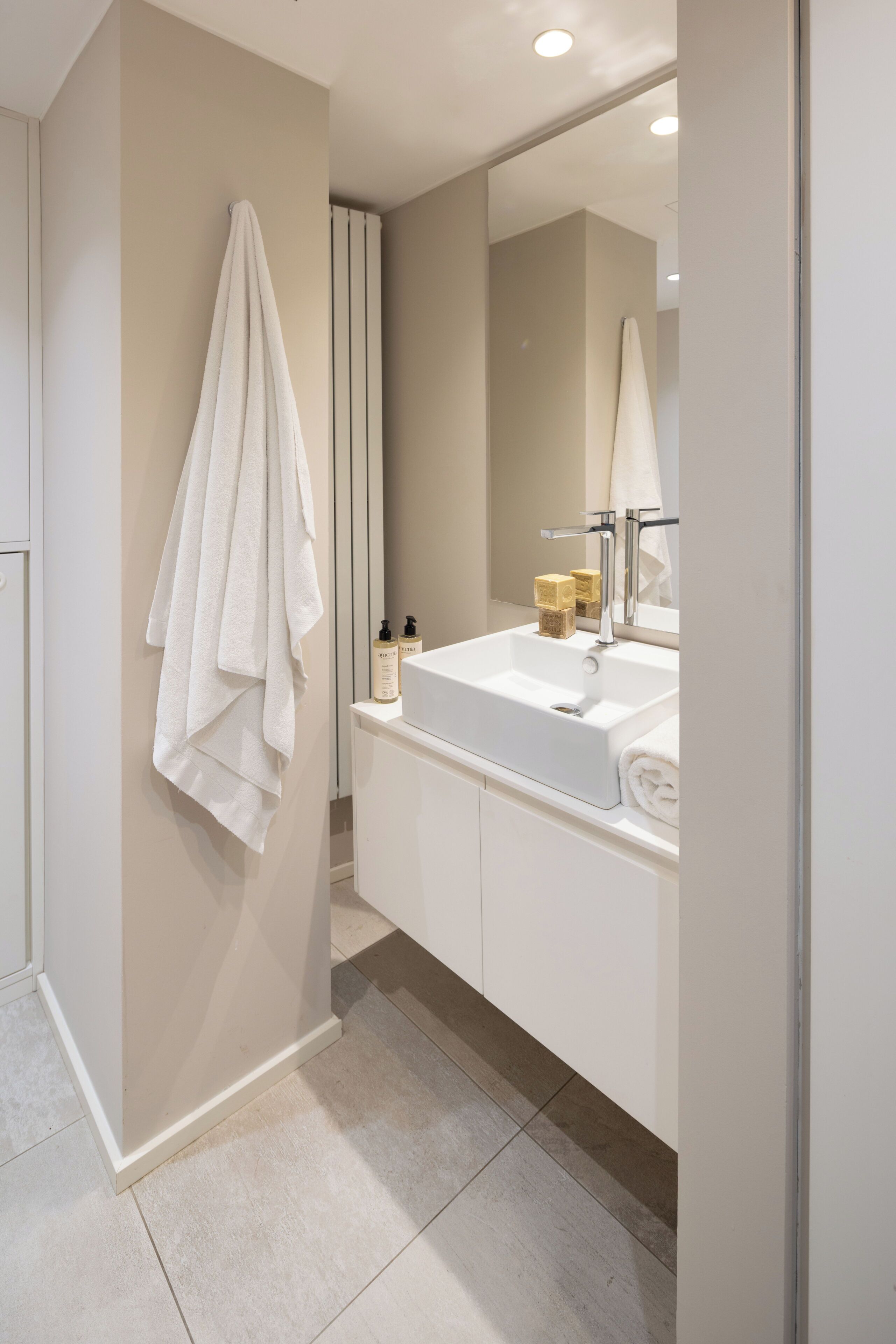 Un baño moderno con un lavamanos blanco, un espejo y una toalla colgada en la pared.