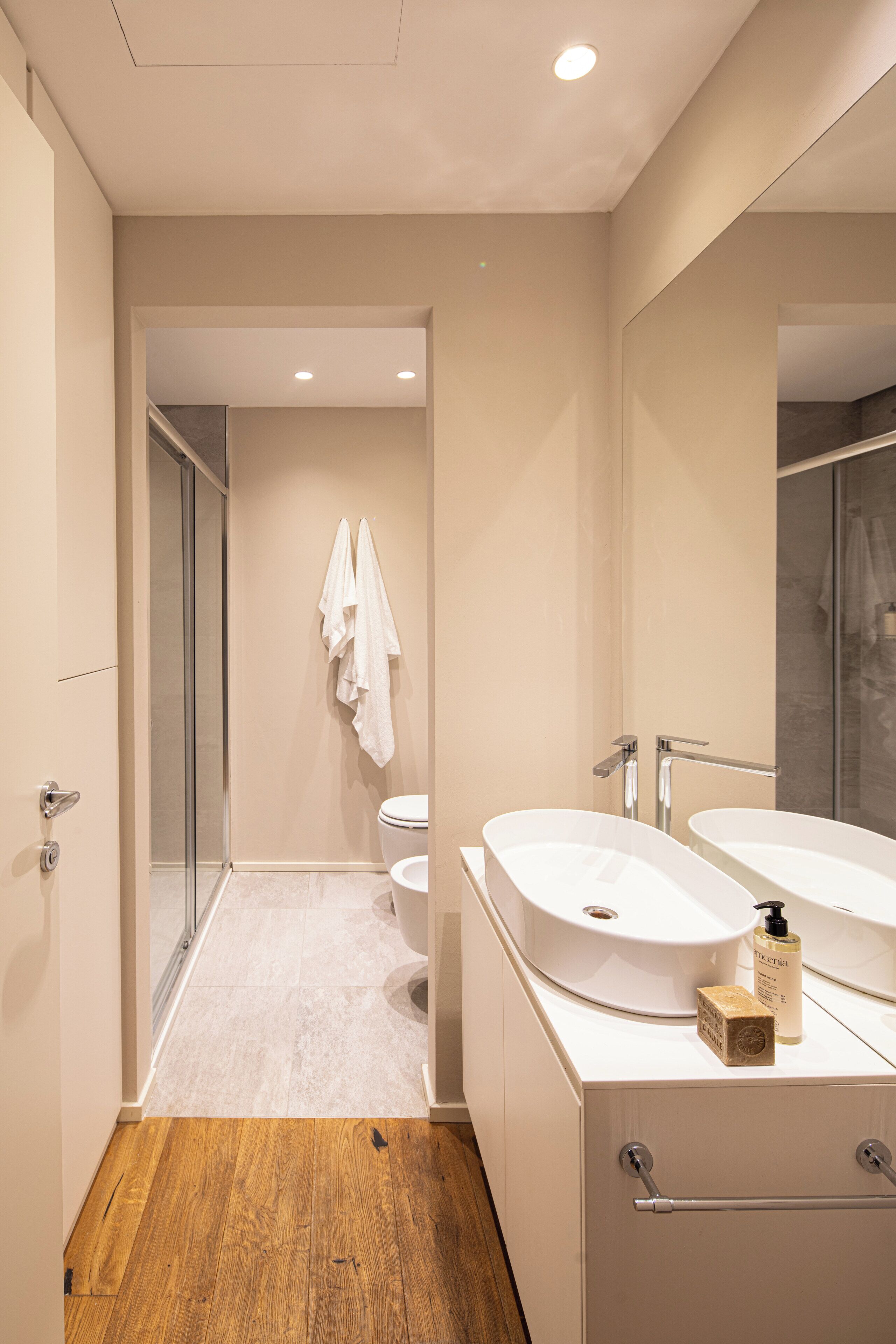 Ein modernes Badezimmer mit Holzboden, zwei Waschbecken, einer Toilette und einer Duschkabine.