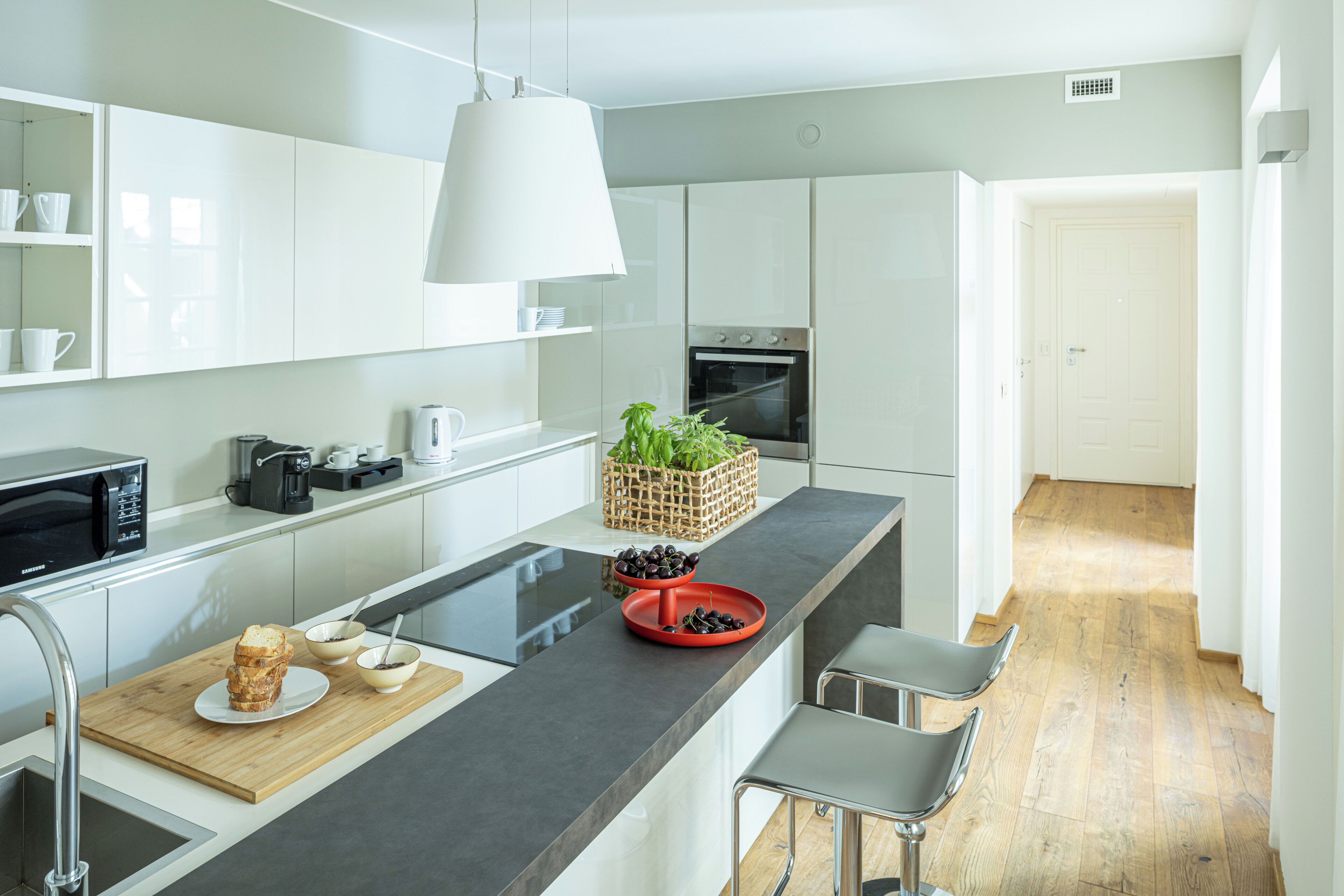 A modern kitchen with white cabinetry, a black countertop, a built-in oven, and a coffee machine.