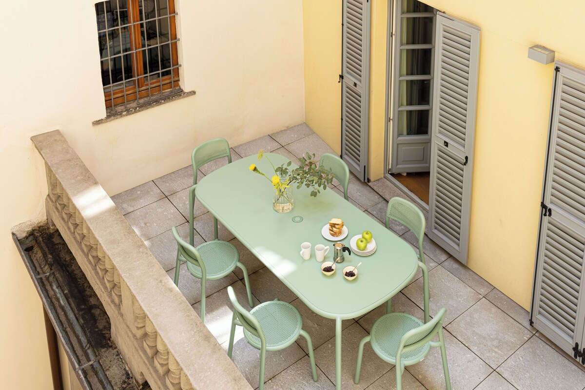Un pequeño espacio exterior con comedor, una mesa, sillas, una ventana con rejas y una puerta con persianas.