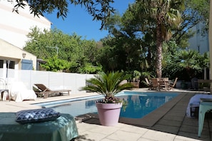 Un espace piscine avec des chaises longues, une plante en pot et un bâtiment en arrière-plan.