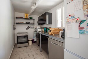 Uma cozinha compacta com fogão, forno, lava-louças e uma televisão preta fixada na parede.