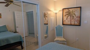 Una camera da letto con un letto, una sedia, una ventola a soffitto, una porta e una lampada fissata al muro.