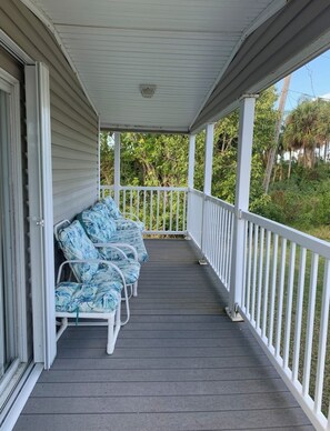 A covered porch with a row of white metal chairs and a white railing. - Charming Sebastian Home Near the Waterfront Activities. (Sebastian)