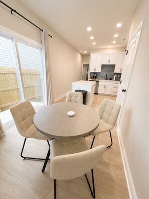A modern kitchen with white cabinets, a central island, and a dining area with a round table and four chairs. - Sleeps 7, 3BD 3BA, 8 minutes to Uptown (Charlotte)