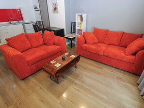 Una sala de estar con dos sofás rojos, una mesa de centro de madera, una mesa de comedor y una zona de cocina con salpicadero rojo.