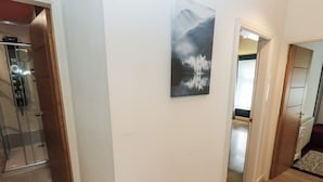 En hall med en dusch av glas, en målning av en fjällsjö och ett trägolv.